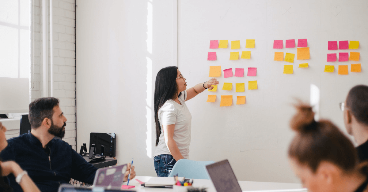 SCRUM Un chica explica los post-its de un tablero kanban agileen una reunión de equipo