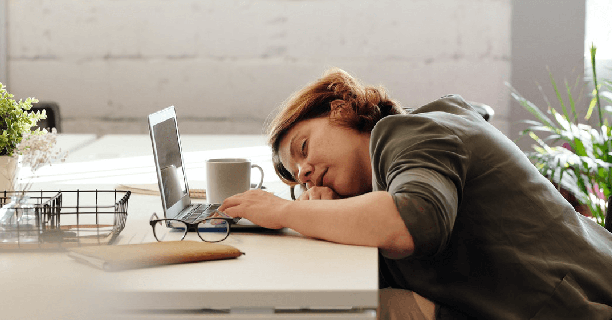 Una chica dormida sobre la mesa frente a su ordenador y una taza de café