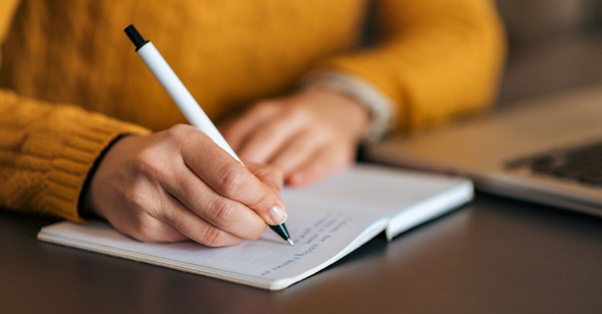 Persona escribiendo en un cuaderno con un bolígrafo sobre UX Writing.